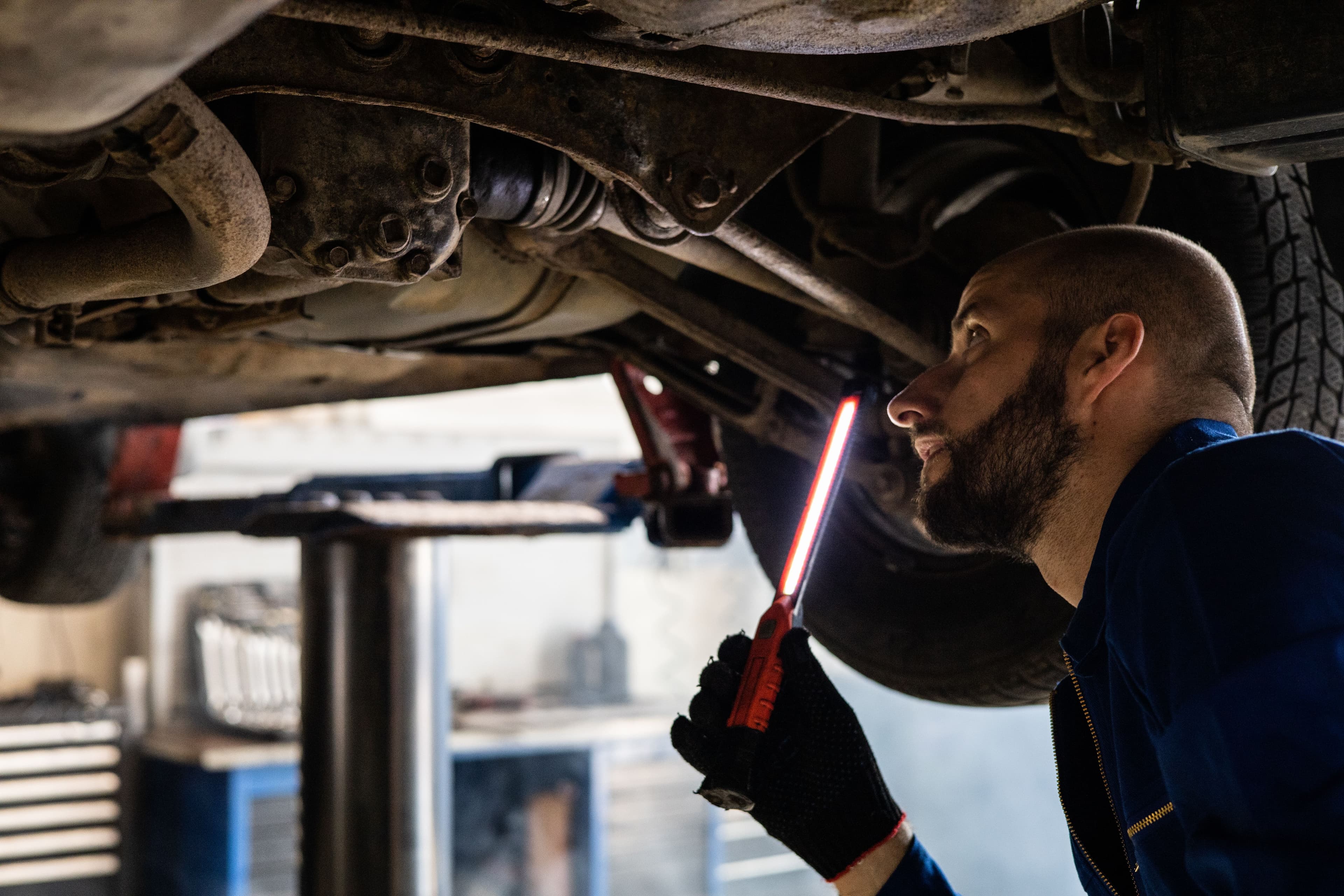 Araç altını özel lambayla inceleyen oto servis teknisyeni